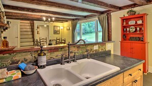 A kitchen with a double sink, wooden beams, a red cabinet with dishes, and a window with a view of greenery. - Historic Hanover Area Home, 16 Miles to Dartmouth! (Enfield)
