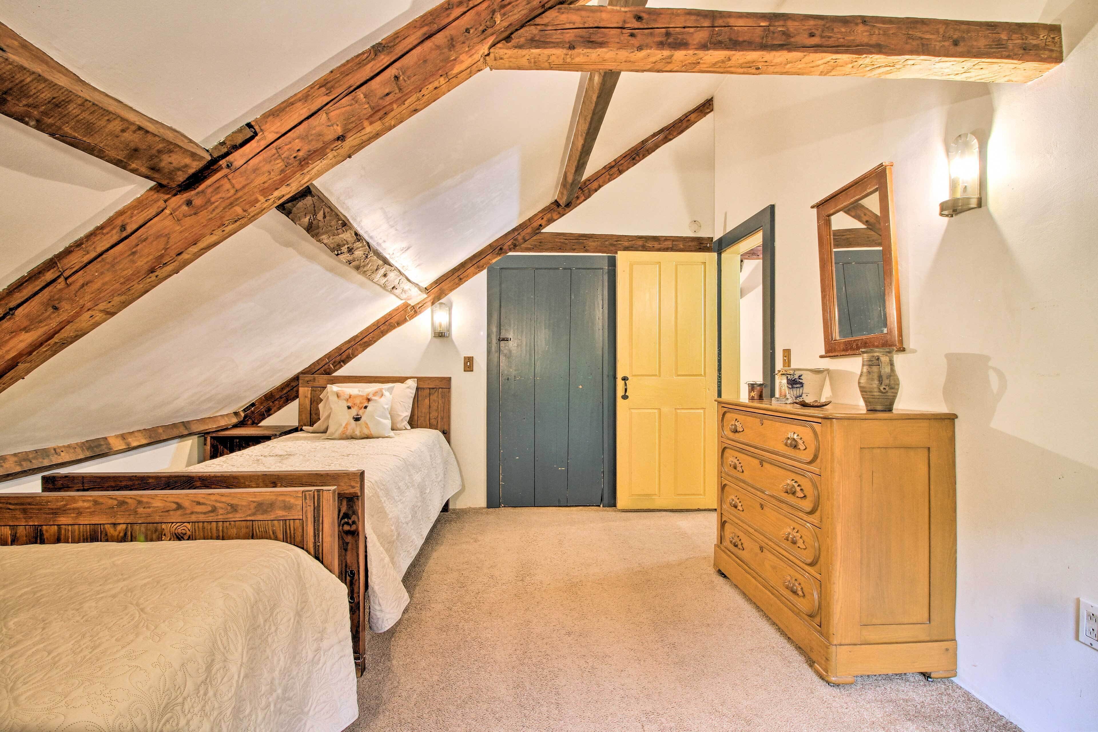 A bedroom with a sloped ceiling, wooden beams, a bed, a dresser, and a door.