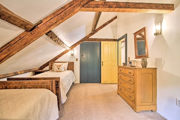 Un dormitorio con techo inclinado, vigas de madera, una cama, un aparador y una puerta.