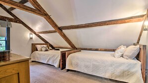 A bedroom with a sloped ceiling, two beds, a wooden dresser, and a nightstand. - Historic Hanover Area Home, 16 Miles to Dartmouth! (Enfield)