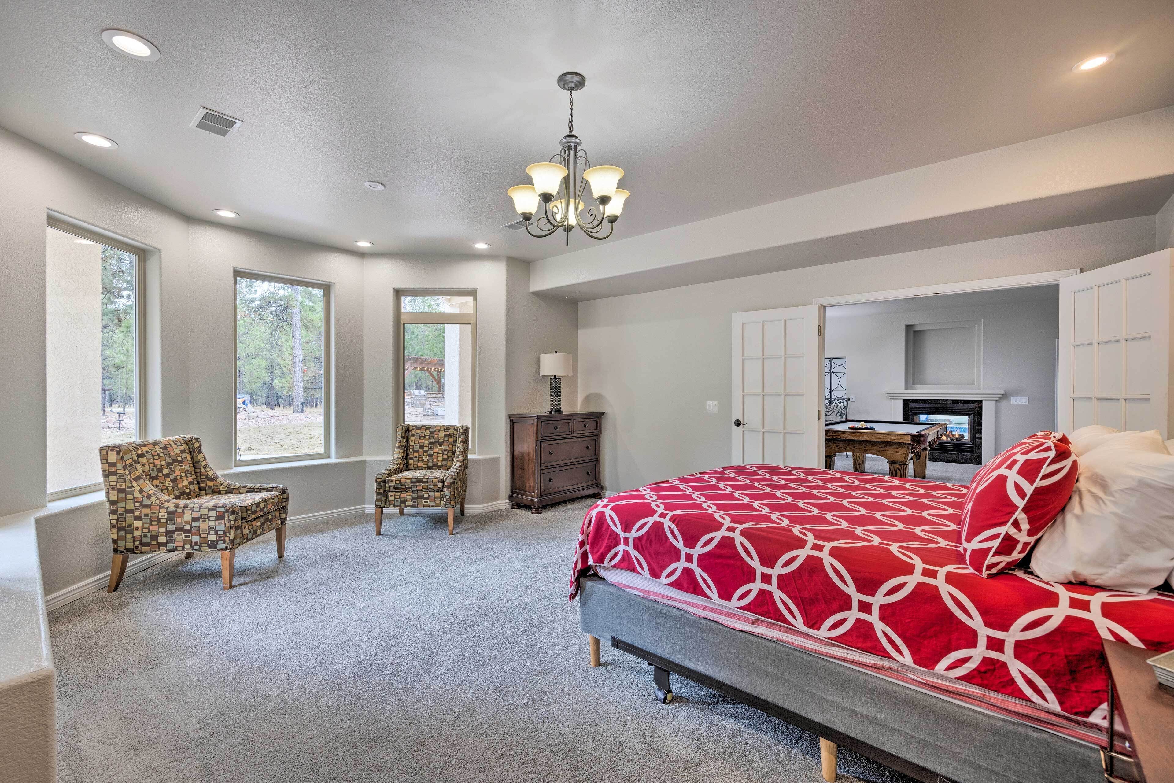 A bedroom with a large bed, two chairs, a dresser, and a fireplace.