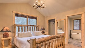 Un dormitorio con estructura de cama de madera, un candelabro, una ventana con persianas y vistas a un baño.