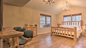 Un dormitorio con una cama de madera, un escritorio, sillas, ventanas amplias y un candelabro.
