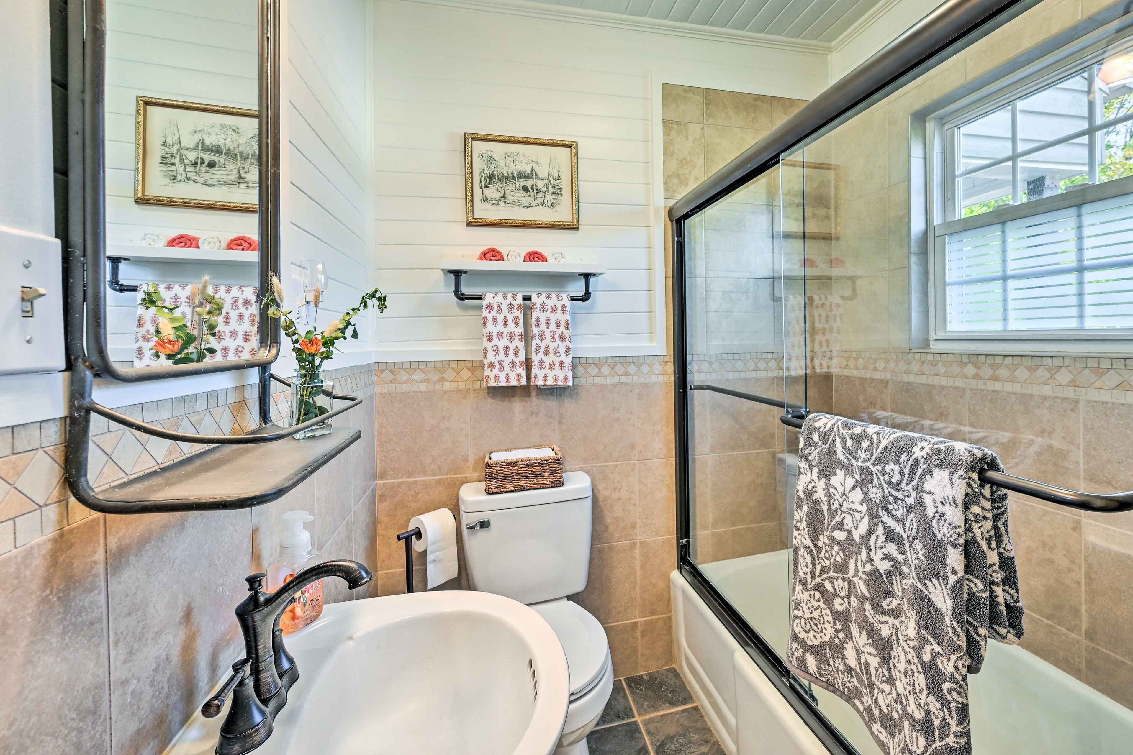 Een badkamer met een wit wastafelmeubel, een toilet, een douche met glazen wanden en twee foto's in lijsten aan de muur.