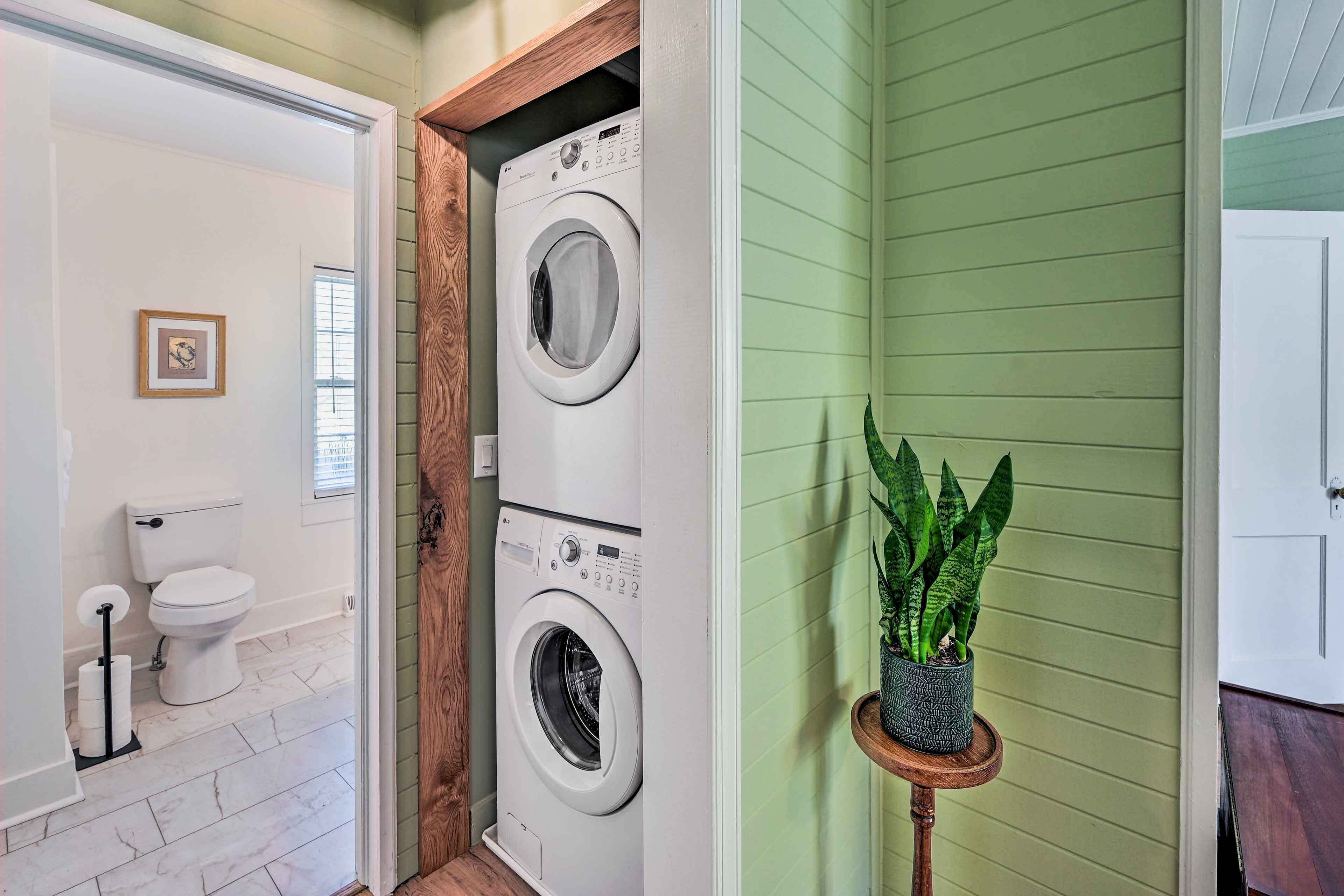 Un cuarto de lavandería con dos lavadoras apiladas, un inodoro y una planta en maceta.