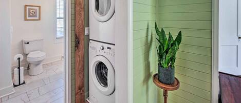 Un cuarto de lavandería con dos lavadoras apiladas, un inodoro y una planta en maceta.