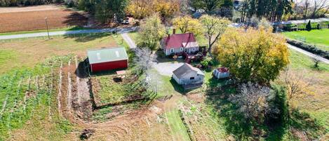An aerial view of a rural property with a main house, a red barn, and a smaller white building. There are fields and trees surrounding the property.