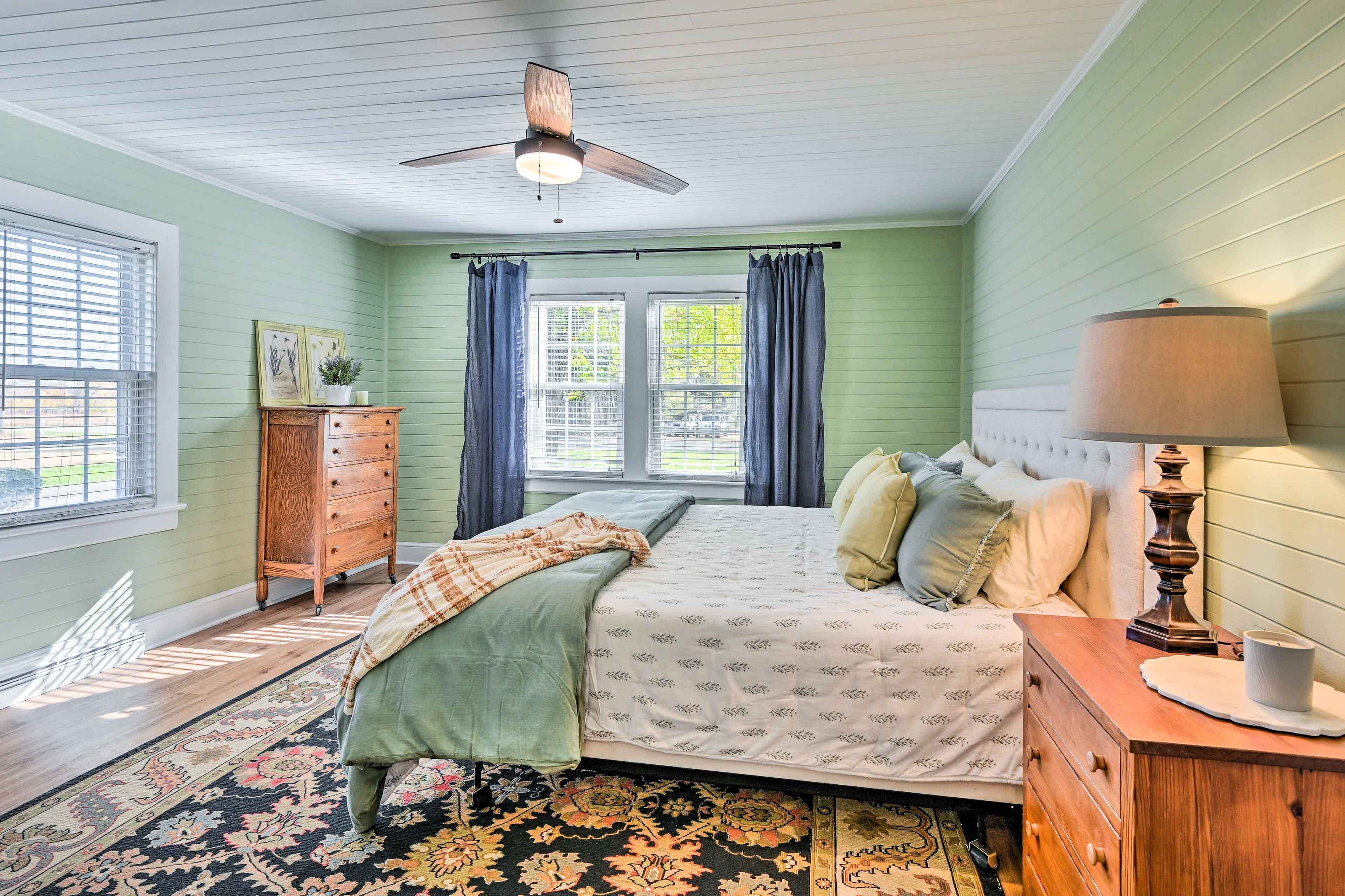 A bedroom with a bed, a dresser, a nightstand, a ceiling fan, and a window with curtains.