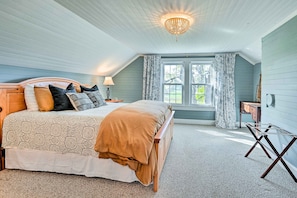 Cozy retreat with a large bed, sloped ceiling, and a window with floral curtains.
