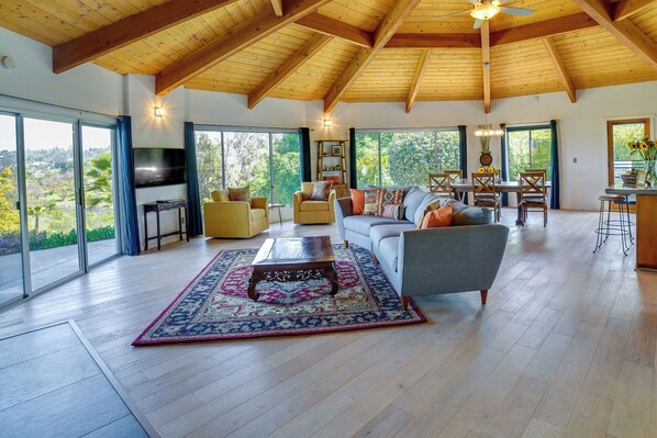 A spacious living room with a wooden ceiling, large windows, a TV, and a dining area with a table and chairs. - Fallbrook Home w/ Mountain Views: Close to Hiking! (Fallbrook)
