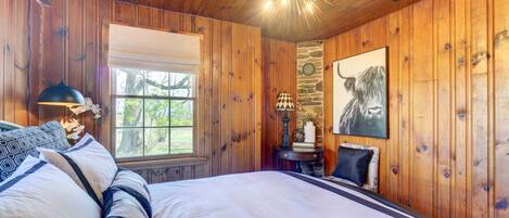 A wooden-paneled bedroom with a large bed, a stone accent wall, a window, and a ceiling light fixture.