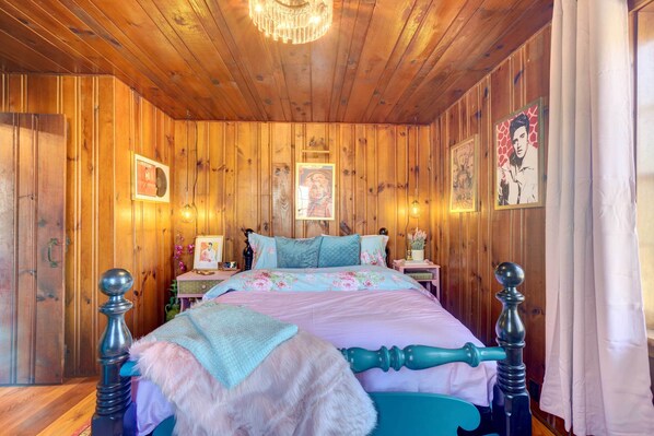 A wooden-paneled bedroom with a bed, decorative pillows, and framed pictures on the walls. - Historic Tennessee Vacation Rental on Homestead (Crossville)