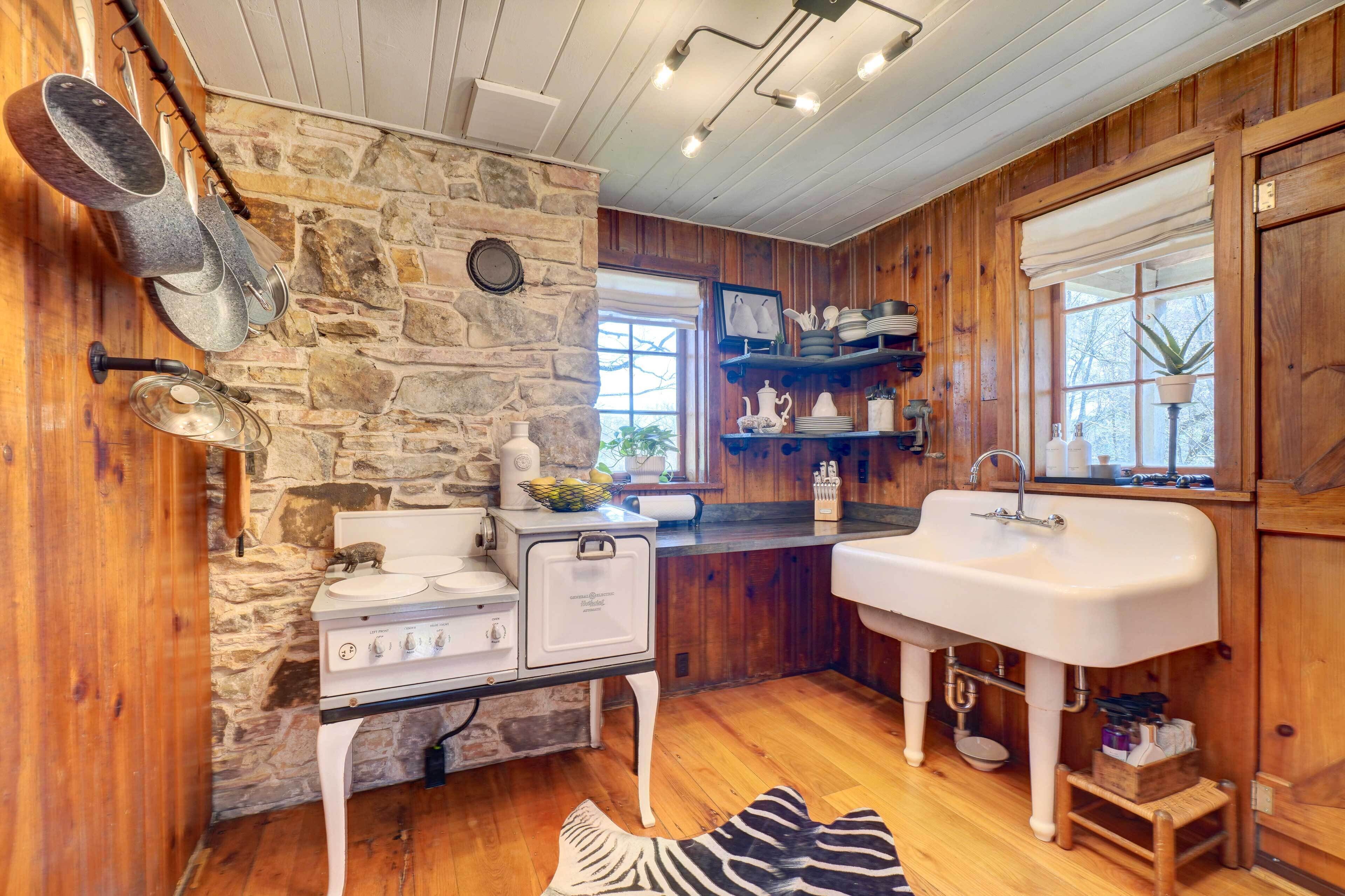 A rustic kitchen with stone walls, wooden cabinets, a white stove, and a large sink.
