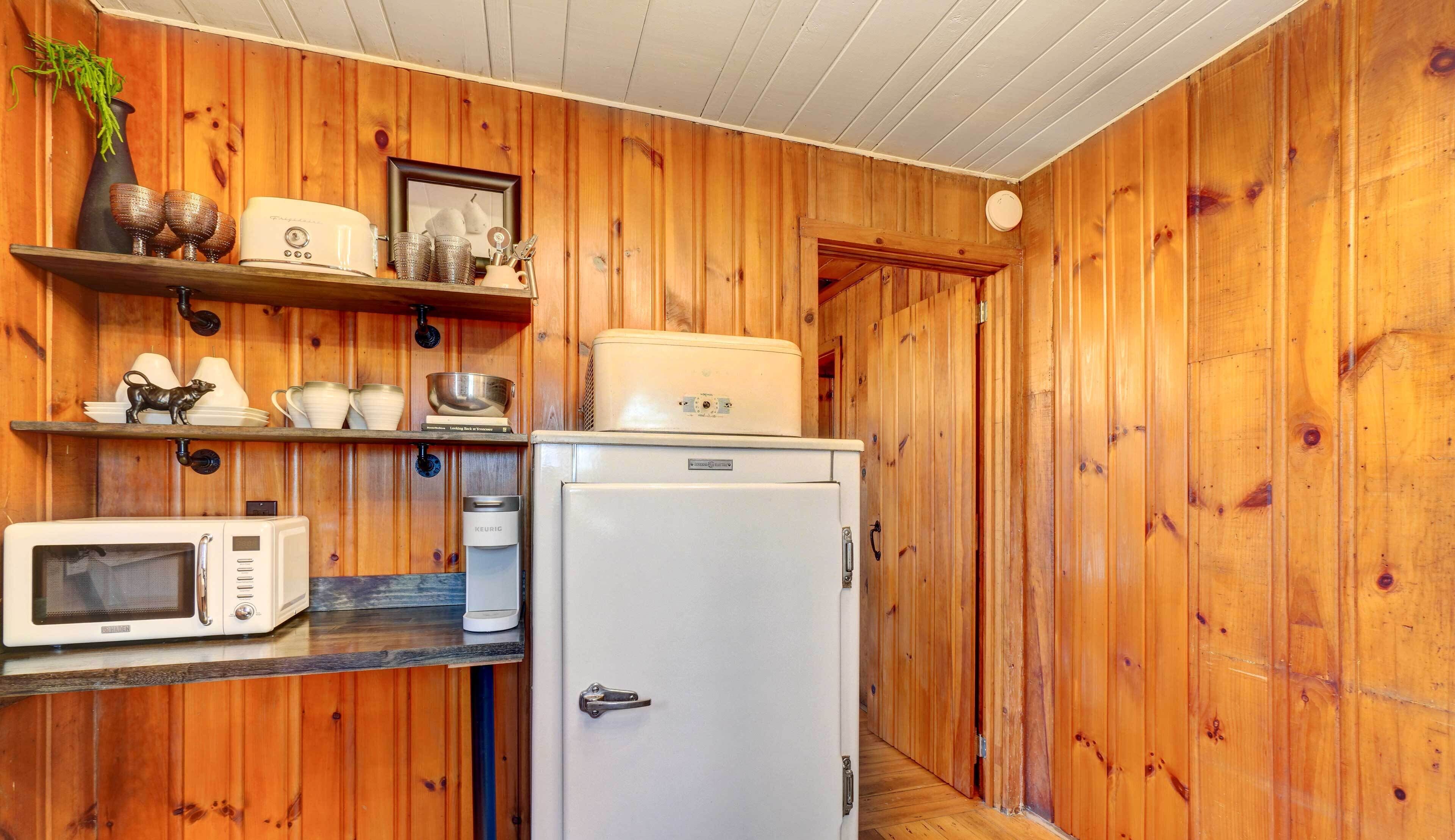 A compact kitchen with wooden walls, a white refrigerator, a microwave, and a coffee maker.