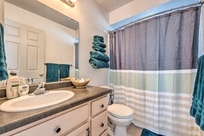 Une salle de bain avec un lavabo, un miroir et des toilettes. Des serviettes sont pliées et empilées sur un porte-serviettes mural, et il y a un rideau de douche à rayures.
