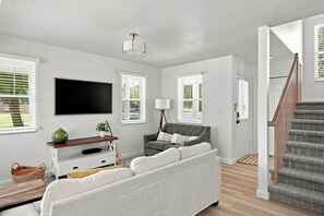 A modern living room with a grey sofa, a flat-screen TV, and a staircase. - Meadow Retreat' Near Parks & USU (Logan)