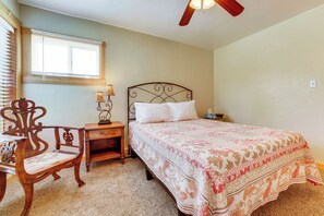 A bedroom with a bed, a chair, a nightstand, a lamp, and a window with blinds.