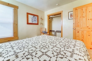 A bedroom with a patterned bedspread, a wooden door, and a window with blinds. - Fruita Vacation Rental: Walk to Downtown! (Fruita)