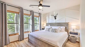 A bedroom with a large bed, a ceiling fan, a wall-mounted deer head decoration, and a nightstand with a lamp. - 'foxtail' Cabin Retreat: Steps to Beaver Lake! (Rogers)
