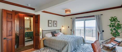 A bedroom with a bed, a chair, a view to the outside, and a door leading to another room.