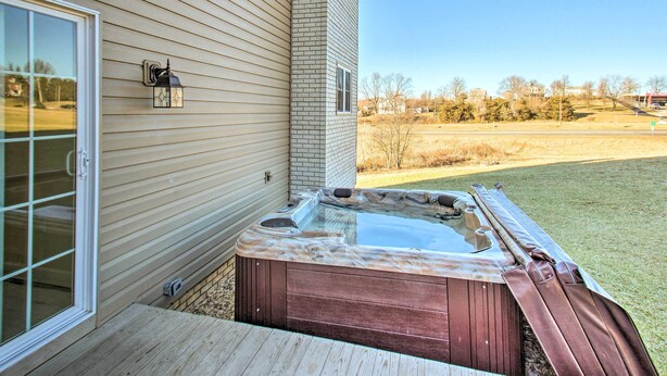Un jacuzzi junto a una casa con terraza de madera y puerta de vidrio.
