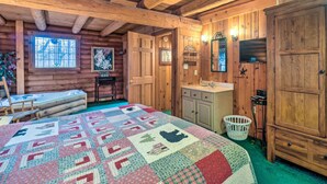 A cozy log cabin room with a large bed, wooden walls, a window, a sink, and a mirror.