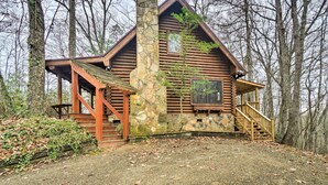 A log cabin with a stone chimney, wooden porch, and a staircase leading to the entrance.