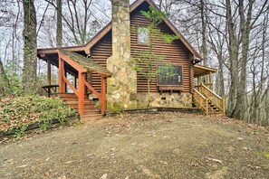 Une cabane en rondins avec une cheminée en pierre, une véranda en bois et un escalier menant à l’entrée.
