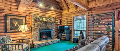 A log cabin interior with a stone fireplace, a television, and a green carpet.