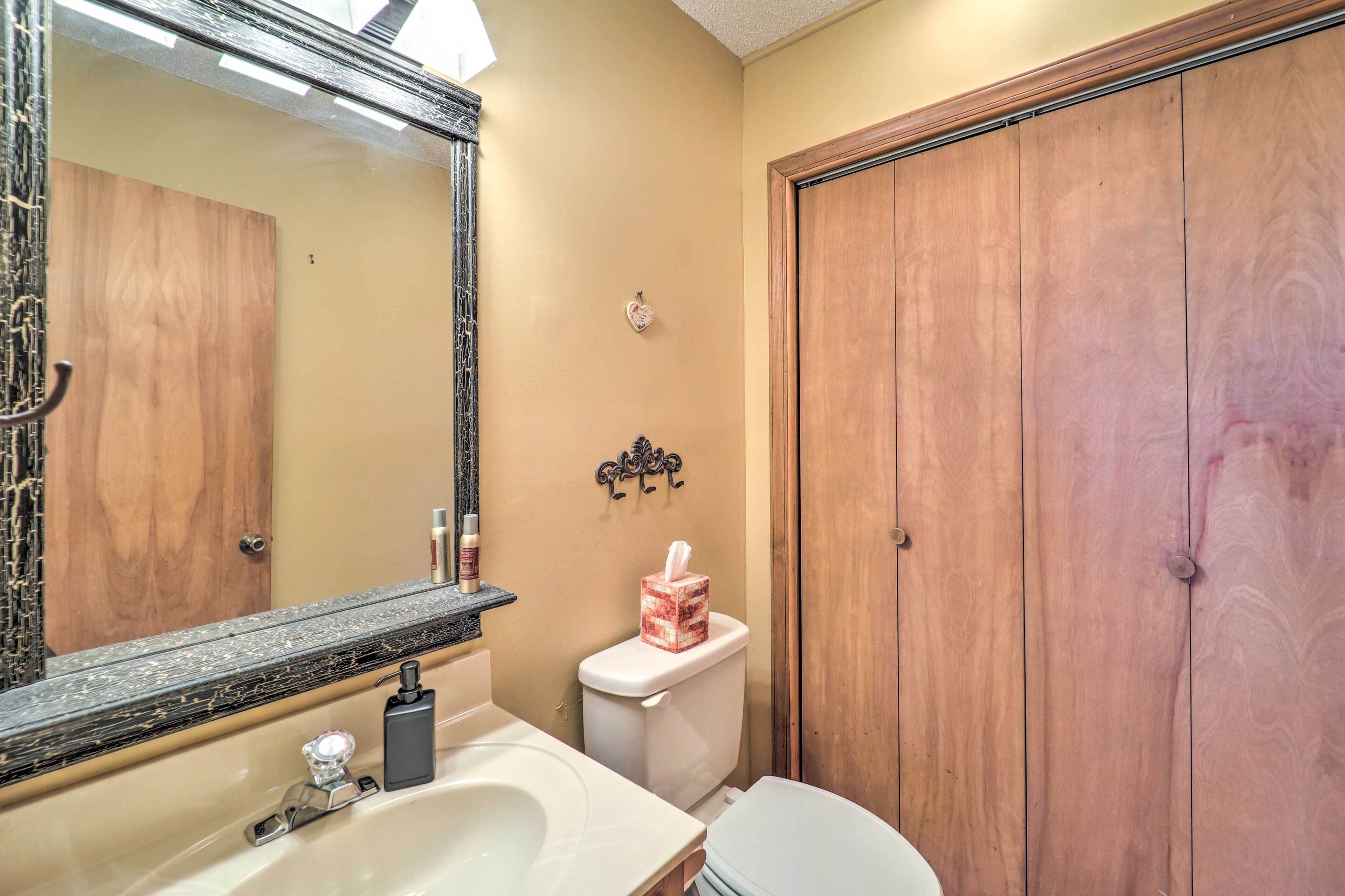 Une salle de bain avec une porte en bois, des toilettes, un lavabo avec un miroir et une boîte de mouchoirs posée sur les toilettes.