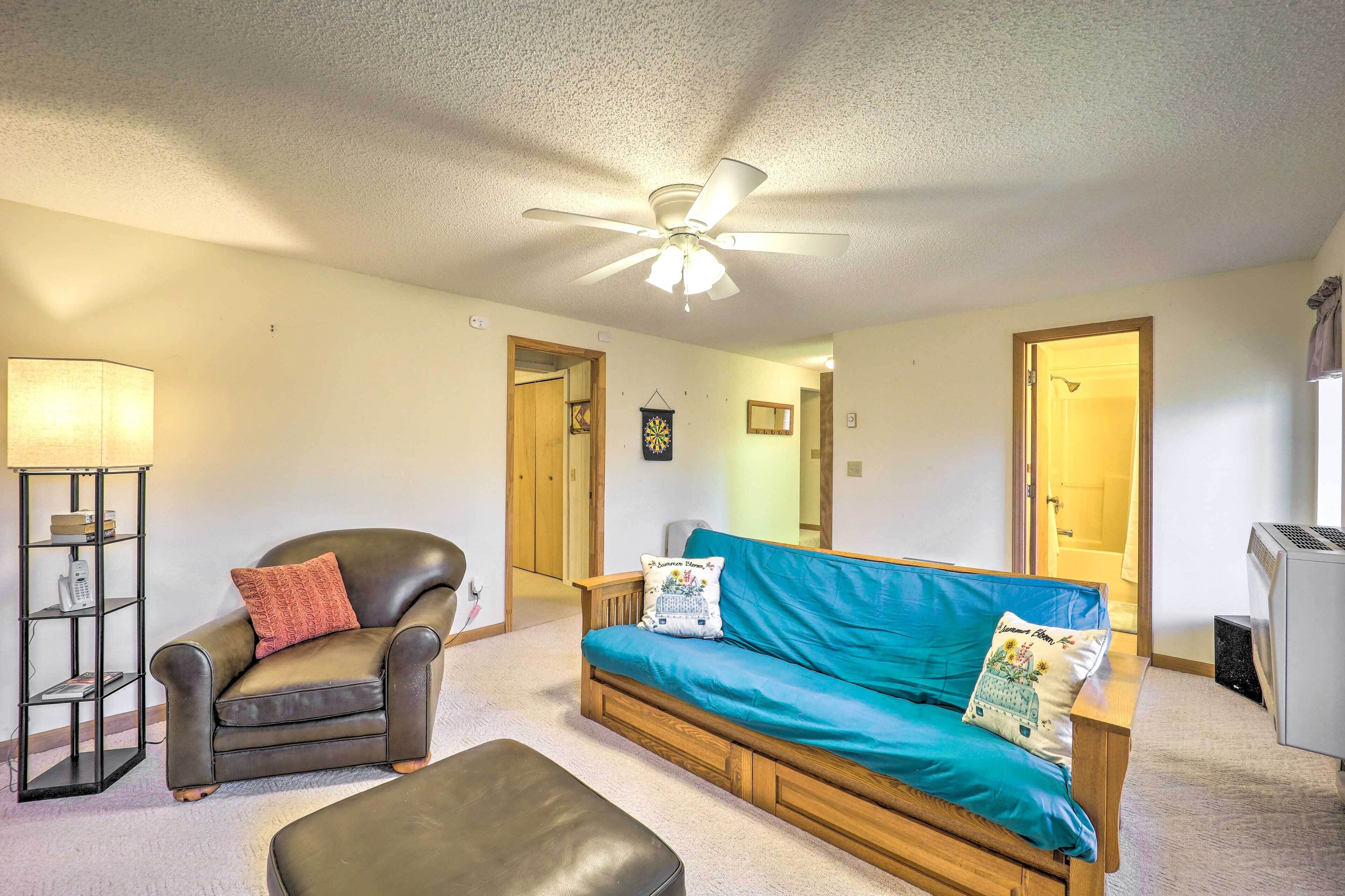 A living room with a ceiling fan, a leather armchair, a blue sofa, and a wooden bench.