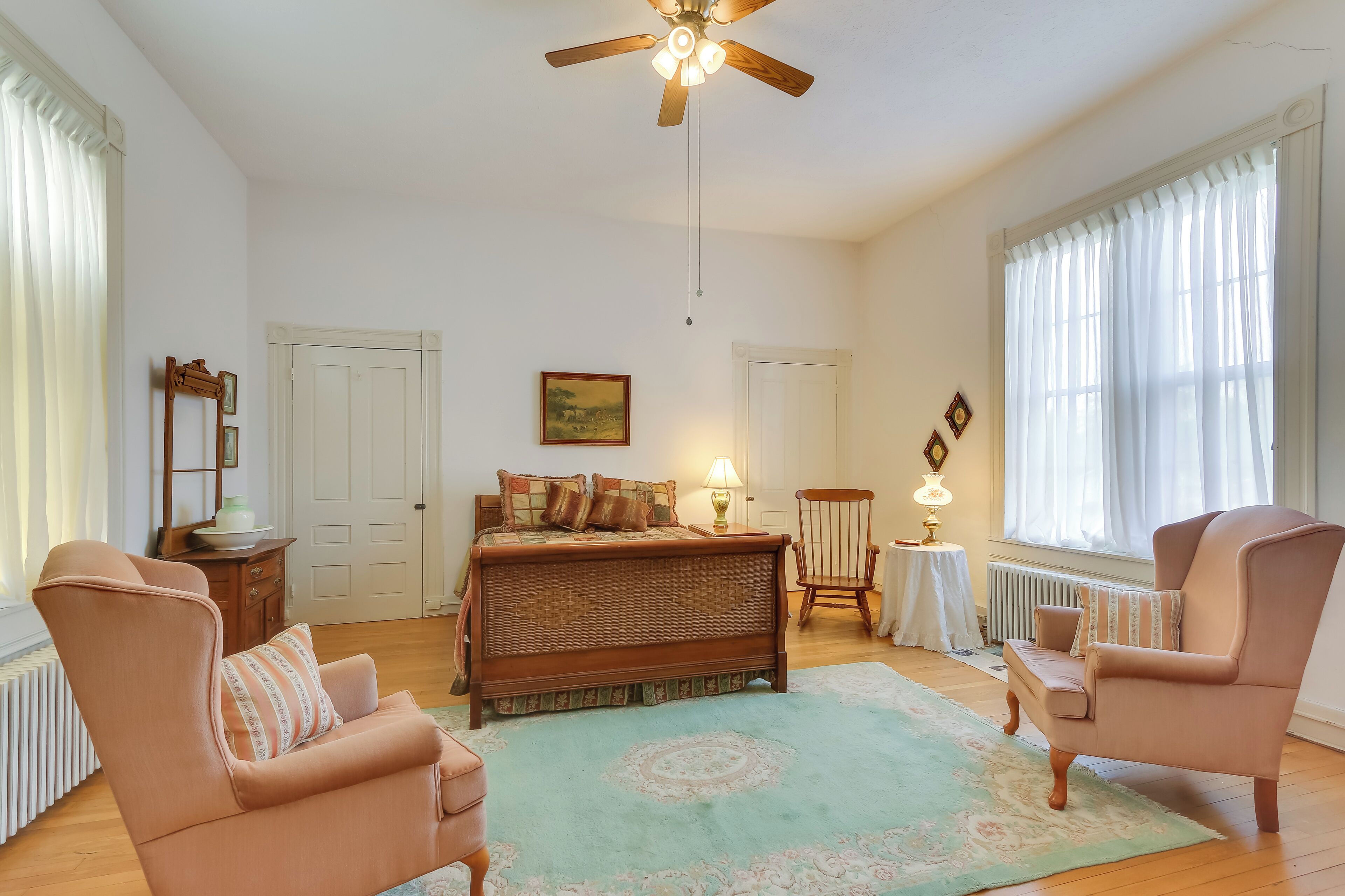 A spacious room with a large bed, two armchairs, a wooden floor, and a ceiling fan.