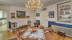 A dining area with a chandelier, wooden chairs, a table set with candles and flowers, and a wall with shelves of dishes. - Historic West Virginia Home Built in 1854! (Moorefield)