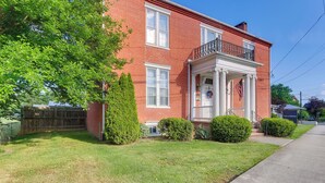A two-story brick house with a front porch, a small front yard, and a mailbox. - Historic West Virginia Home Built in 1854! (Moorefield)