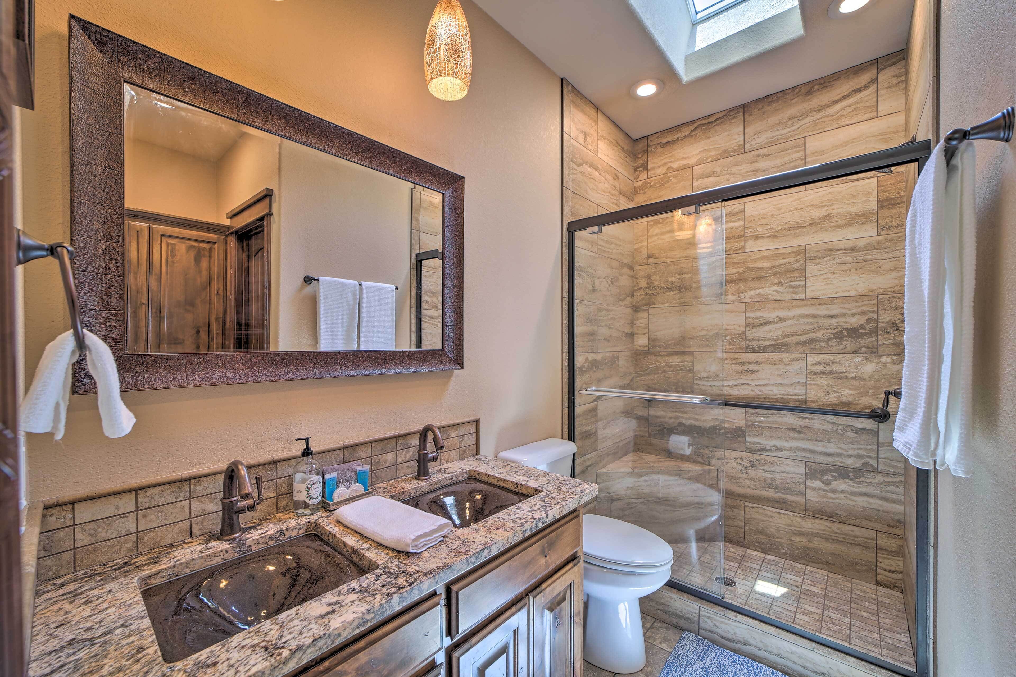 A modern bathroom with a granite sink, a large mirror, a glass-enclosed shower, and a toilet.