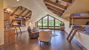Une chambre spacieuse de style « loft », avec de hauts plafonds, des poutres en bois et de grandes fenêtres offrant une vue sur l’extérieur.