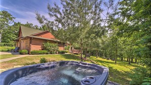 Un bain à remous dans un cadre extérieur luxuriant et verdoyant, avec un chalet en bois en arrière-plan.