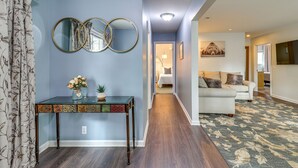 A hallway with a glass console table, two wall mirrors, a floral vase, and a patterned rug leading to a living area with a sofa and a painting. - 'house in the Woods' in Ooltewah w/ Fire Pit! (Ooltewah)