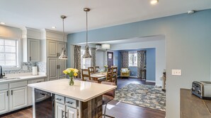 A modern kitchen with a central island, dining area with chairs, and a living room with a sofa. - 'house in the Woods' in Ooltewah w/ Fire Pit! (Ooltewah)