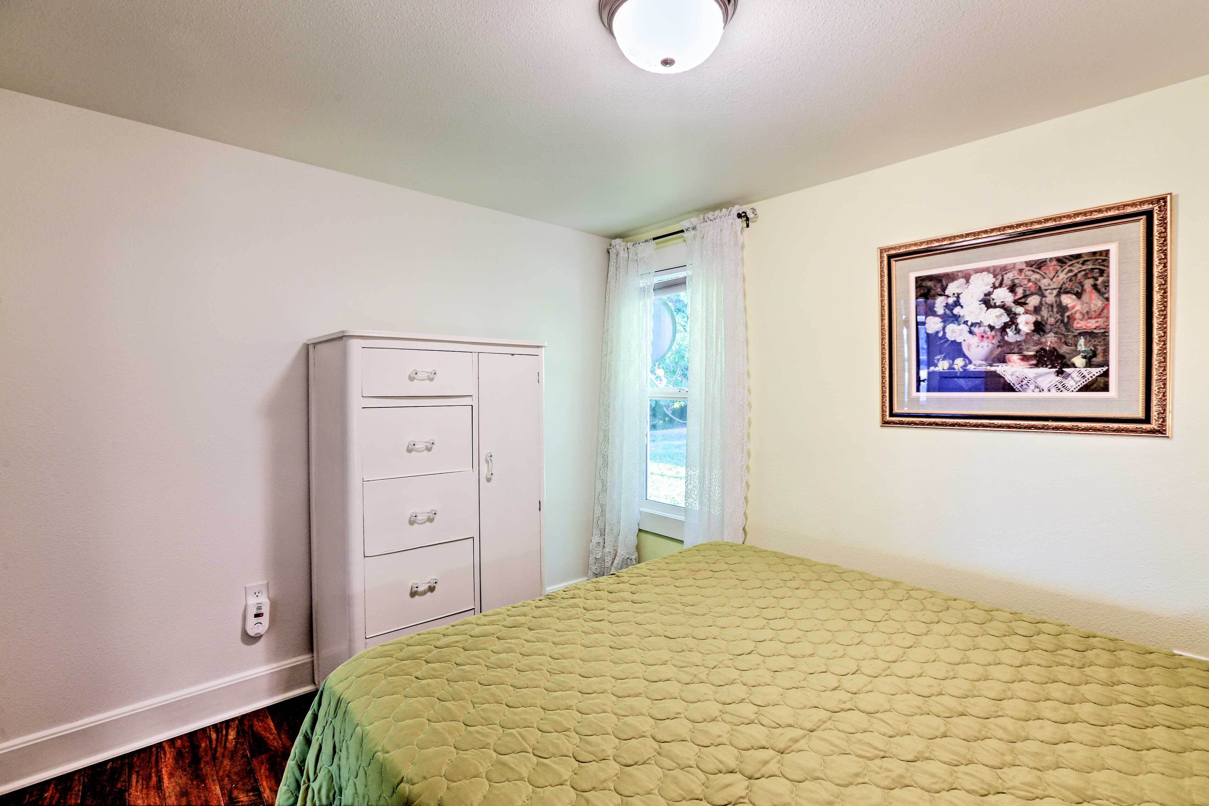 A bedroom with a bed, a dresser, a window with curtains, and a framed picture on the wall.