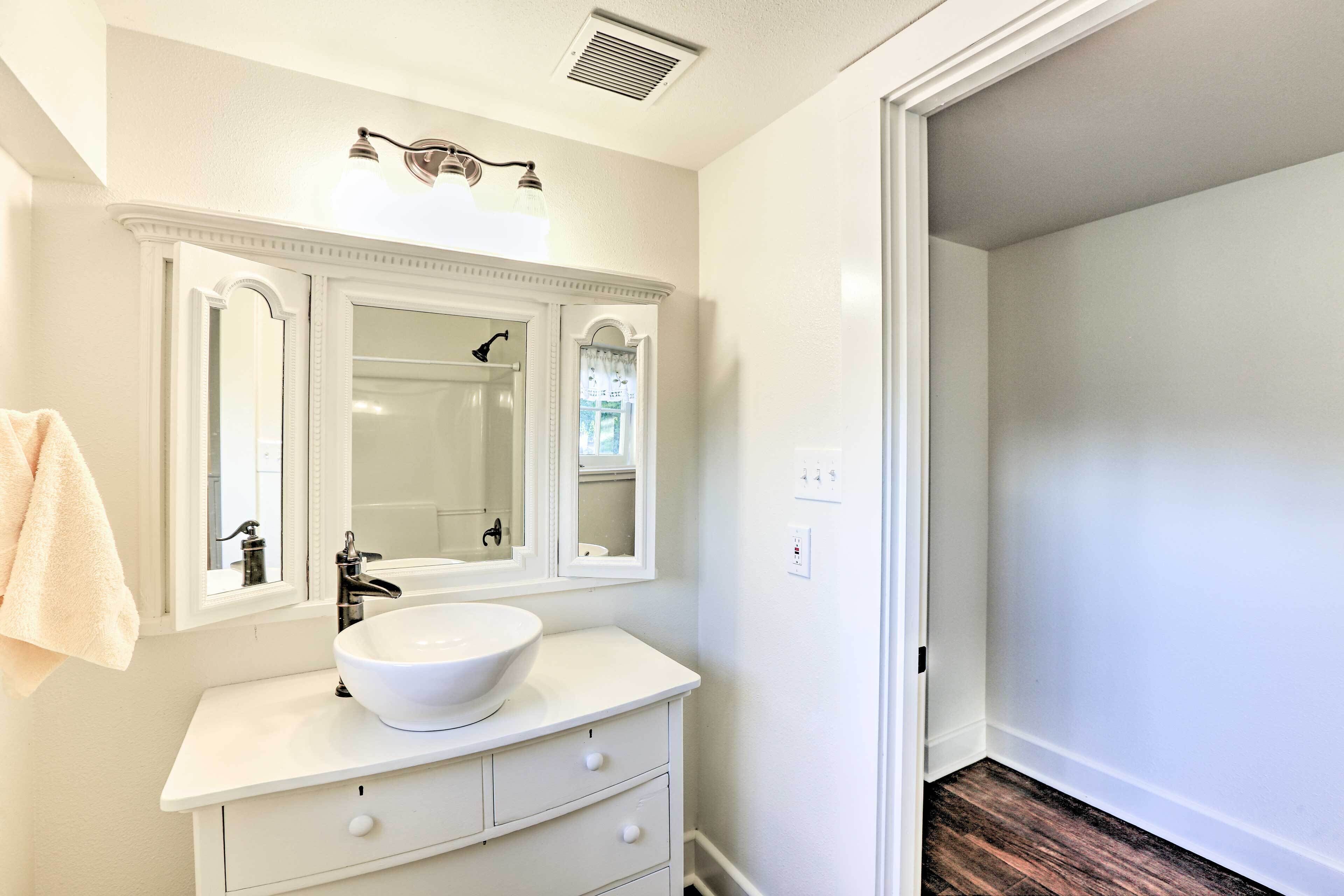 A bathroom with a white vanity, a large mirror, and a white sink.