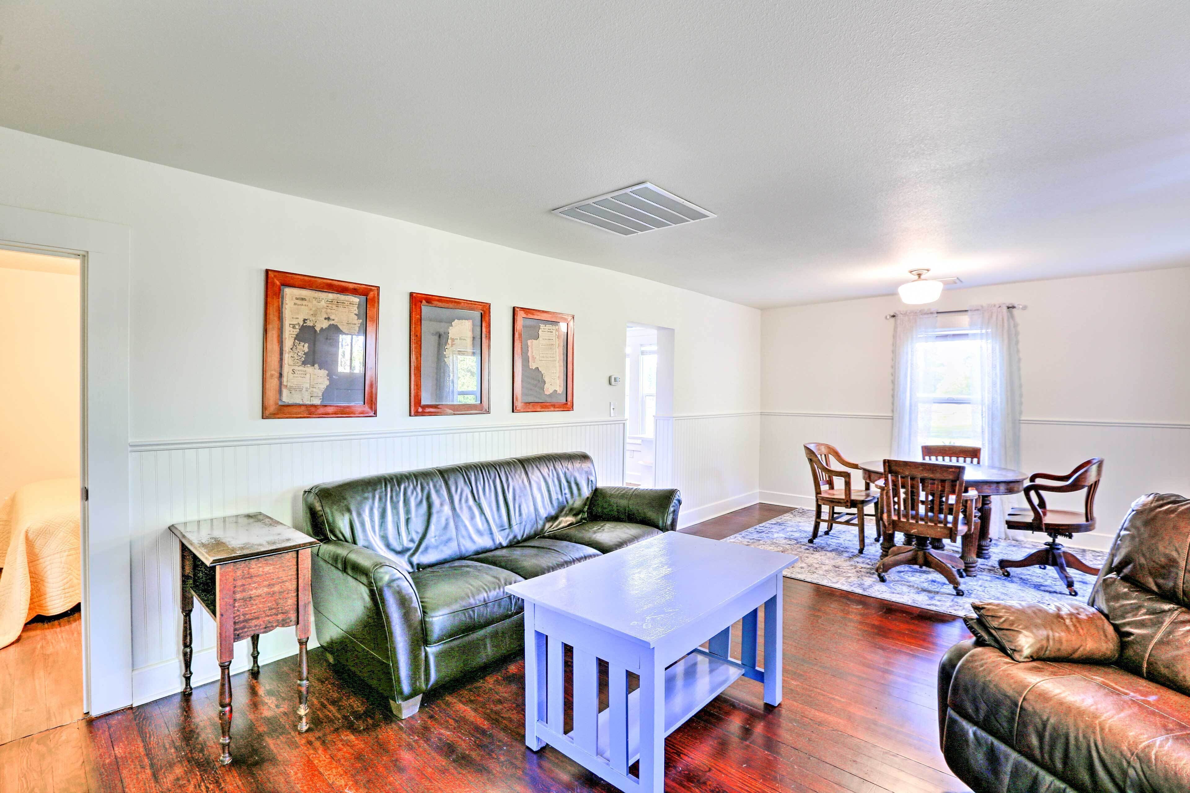 A living room with a green leather sofa, a wooden coffee table, and a dining area with wooden chairs and a table.