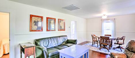 A living room with a green leather sofa, a wooden coffee table, and a dining area with wooden chairs and a table.