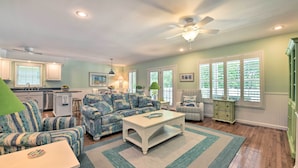 A living room with a sofa, coffee table, and a rug. There is a kitchen area in the background with a window and a ceiling fan. - Lake Norman Retreat w/ Dock ~ 1 Mi to Marina! (Mooresville)