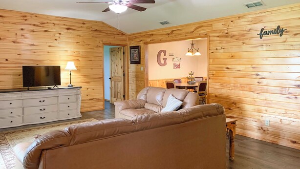 A cozy living room with a leather sofa, a TV on a dresser, and a dining area in the background. - Emory Escape w/ Pond Access < 13 Mi to Lake! (Emory)
