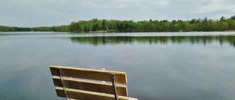 A wooden dock with a bench extending into a calm lake, surrounded by trees.