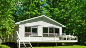 Une cabane de plain-pied dotée d’un porche à l’avant et d’une petite terrasse, entourée d’arbres verdoyants.