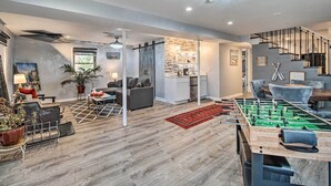 A modern living room with a foosball table, a sofa, a coffee table, and a dining area with chairs. - Sauna & Game Room: Lake House in Locust Grove! (Locust Grove)