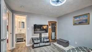 A bedroom with a bed, a TV, a storage unit, and a door leading to a bathroom. - Sauna & Game Room: Lake House in Locust Grove! (Locust Grove)