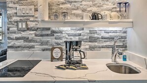 A kitchen with a stone backsplash, a coffee maker, a sink, and a sign that reads "Our Little Coffee Bar". - Sauna & Game Room: Lake House in Locust Grove! (Locust Grove)